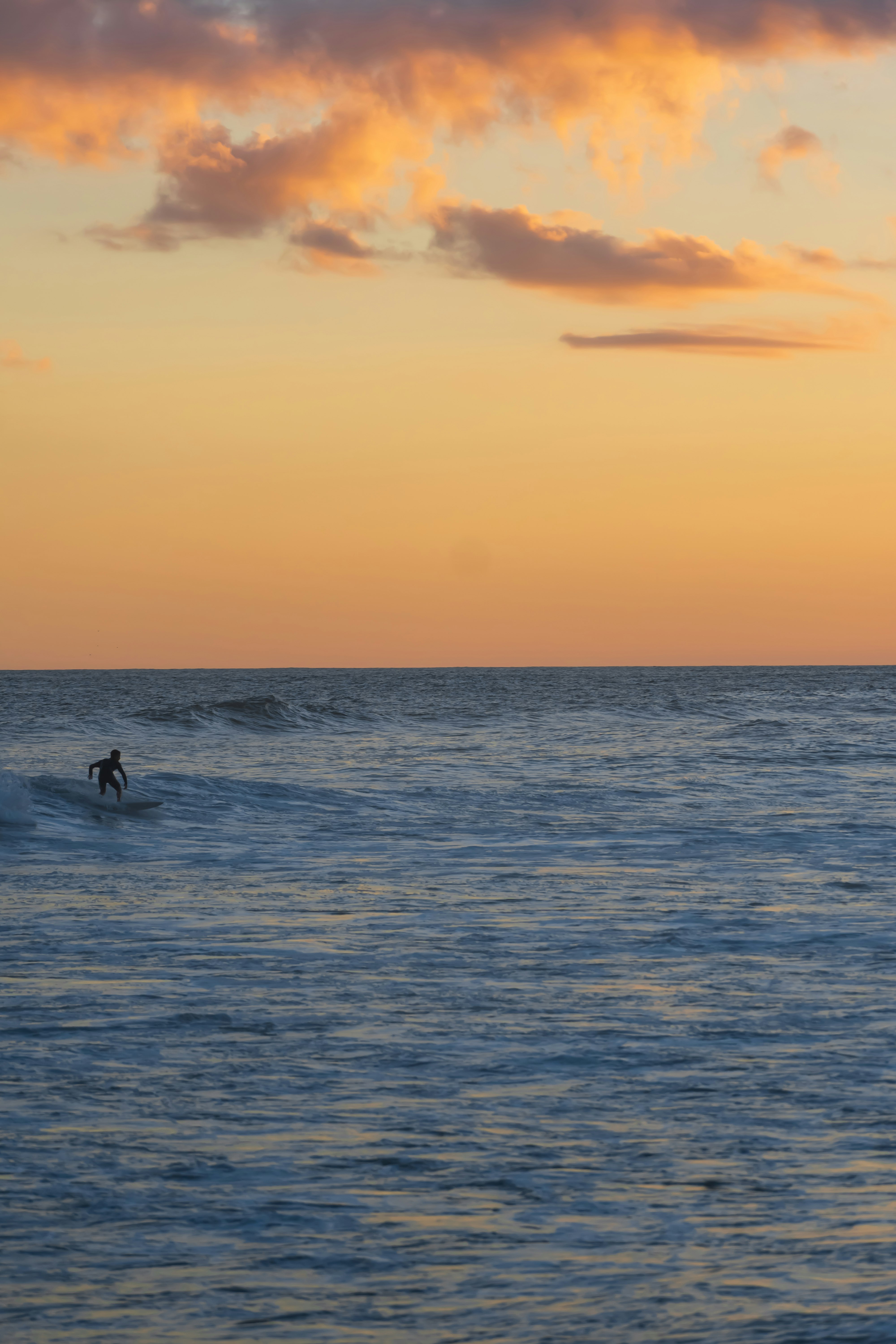 2 people surfing on sea during sunset